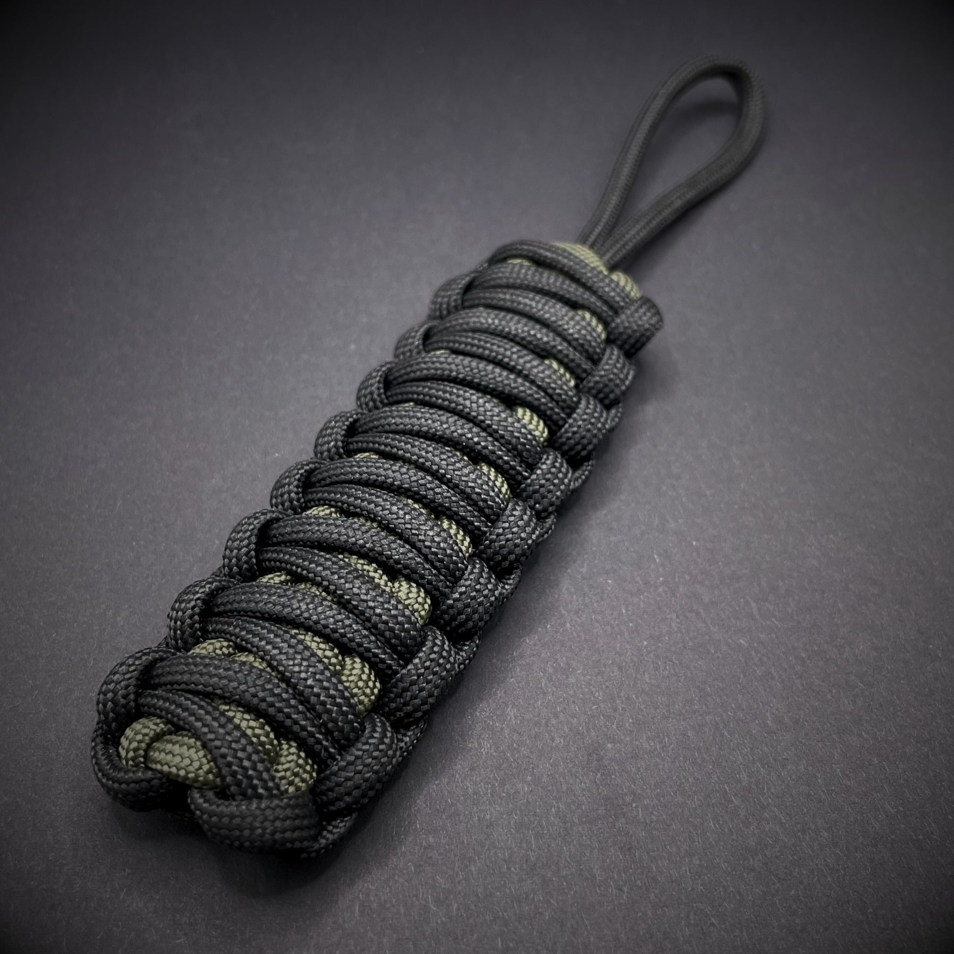 Flat lay of a black and army green 550 Paracord knife lanyards  on a dark grey background