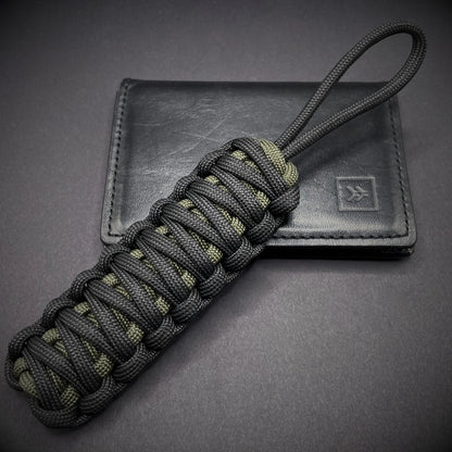 Flat lay of a black and army green 550 Paracord knife lanyards  on a dark grey background