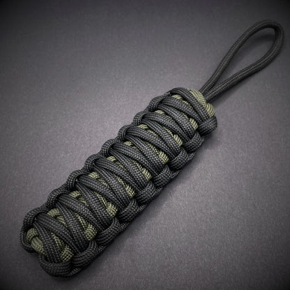 Flat lay of a black and army green 550 Paracord knife lanyards  on a dark grey background