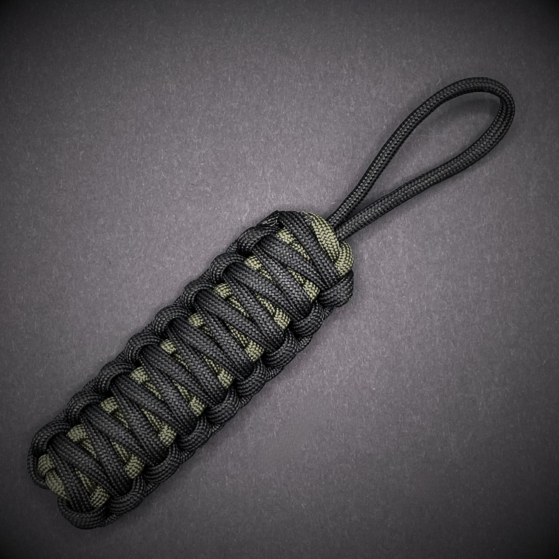 Flat lay of a black and army green 550 Paracord knife lanyards  on a dark grey background