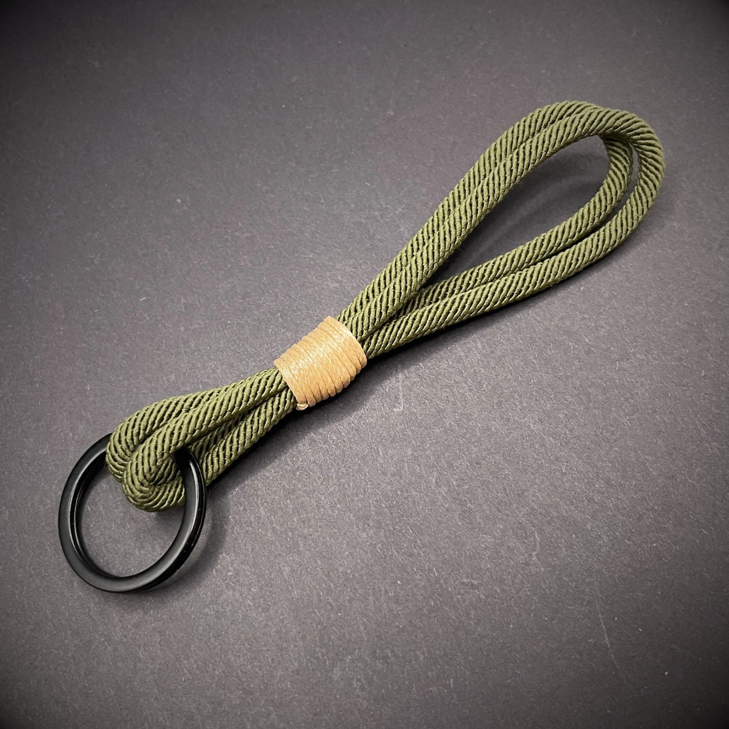 Flat lay of Green Milan Rope keychain with tan cotton whipping on a dark background.
