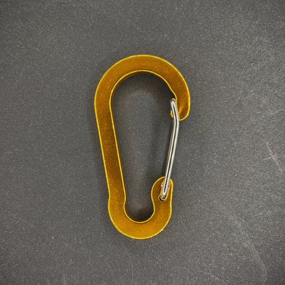 Yellow Anodised aluminium carabiner, arranged on a dark surface.