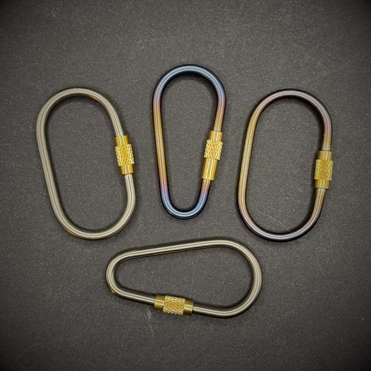 A selection of Mini Locking Titanium Carabiners arranged on a dark surface.