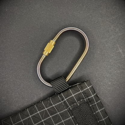 Mini Locking Titanium Carabiner attached to a black grid-patterned pouch, arranged on a dark surface.