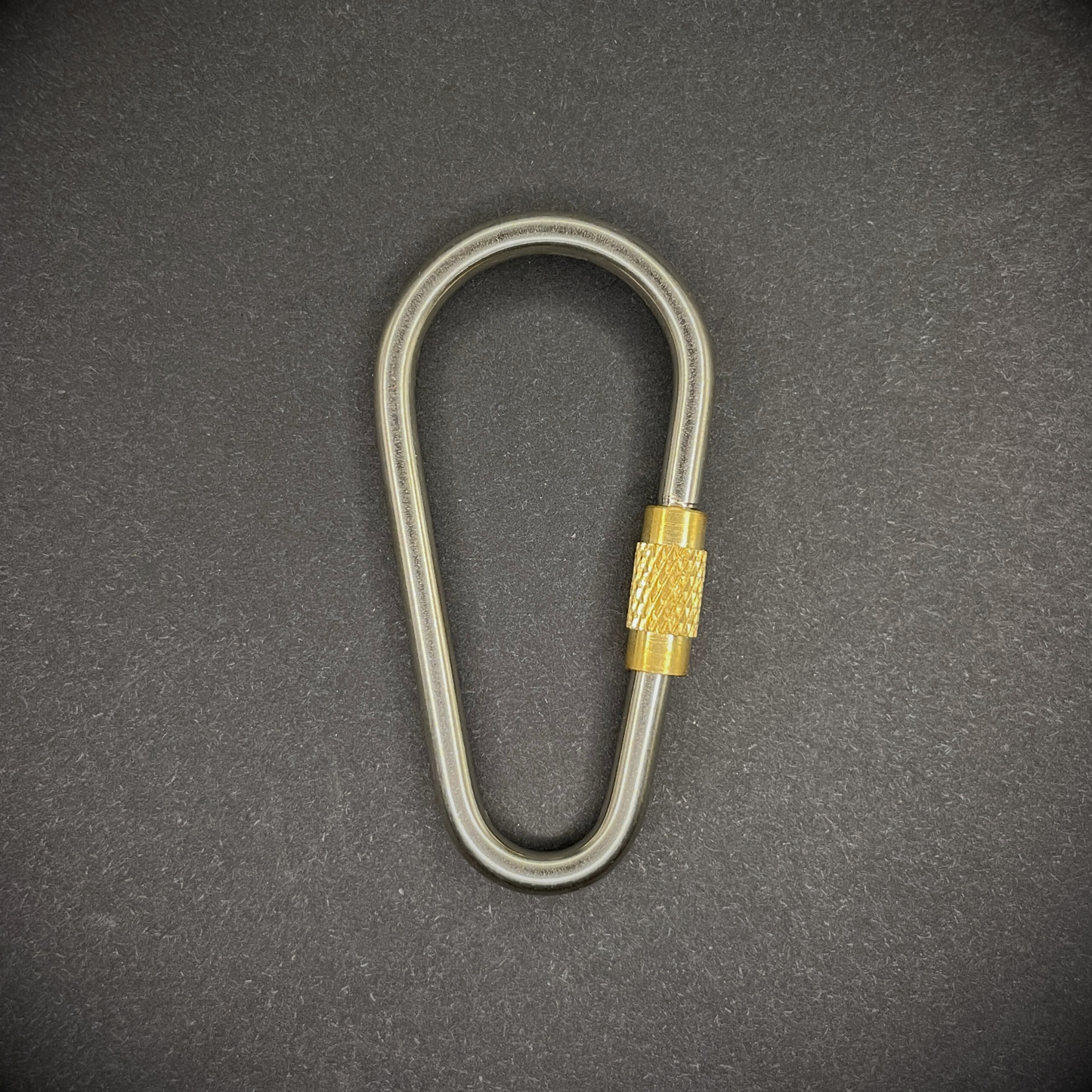 Mini Locking Titanium Carabiner arranged on a dark surface.