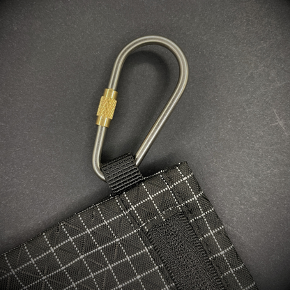 Mini Locking Titanium Carabiner attached to a black grid-patterned pouch, arranged on a dark surface.