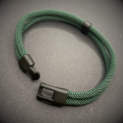 Green rope bracelet with a black metal side-release buckle and minimalist loop detail, displayed on a dark background.