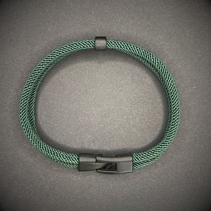 Green rope bracelet with a black metal side-release buckle and minimalist loop detail, displayed on a dark background.