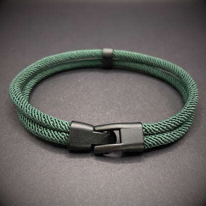 Green rope bracelet with a black metal side-release buckle and minimalist loop detail, displayed on a dark background.