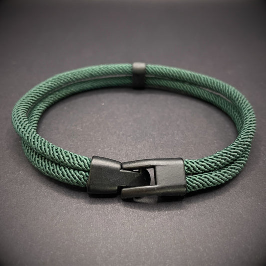 Green rope bracelet with a black metal side-release buckle and minimalist loop detail, displayed on a dark background.