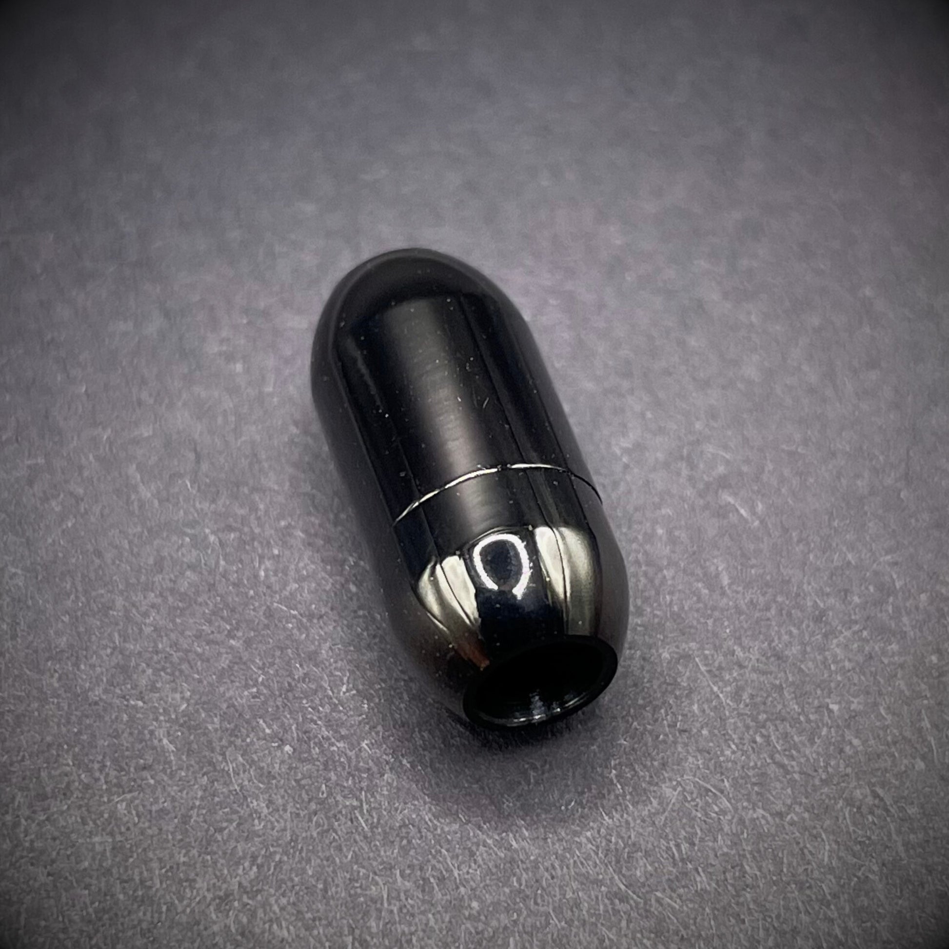 Black cylindrical metal magnetic bracelet clasp, displayed on a dark textured background.