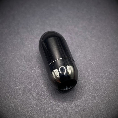 Black cylindrical metal magnetic bracelet clasp, displayed on a dark textured background.