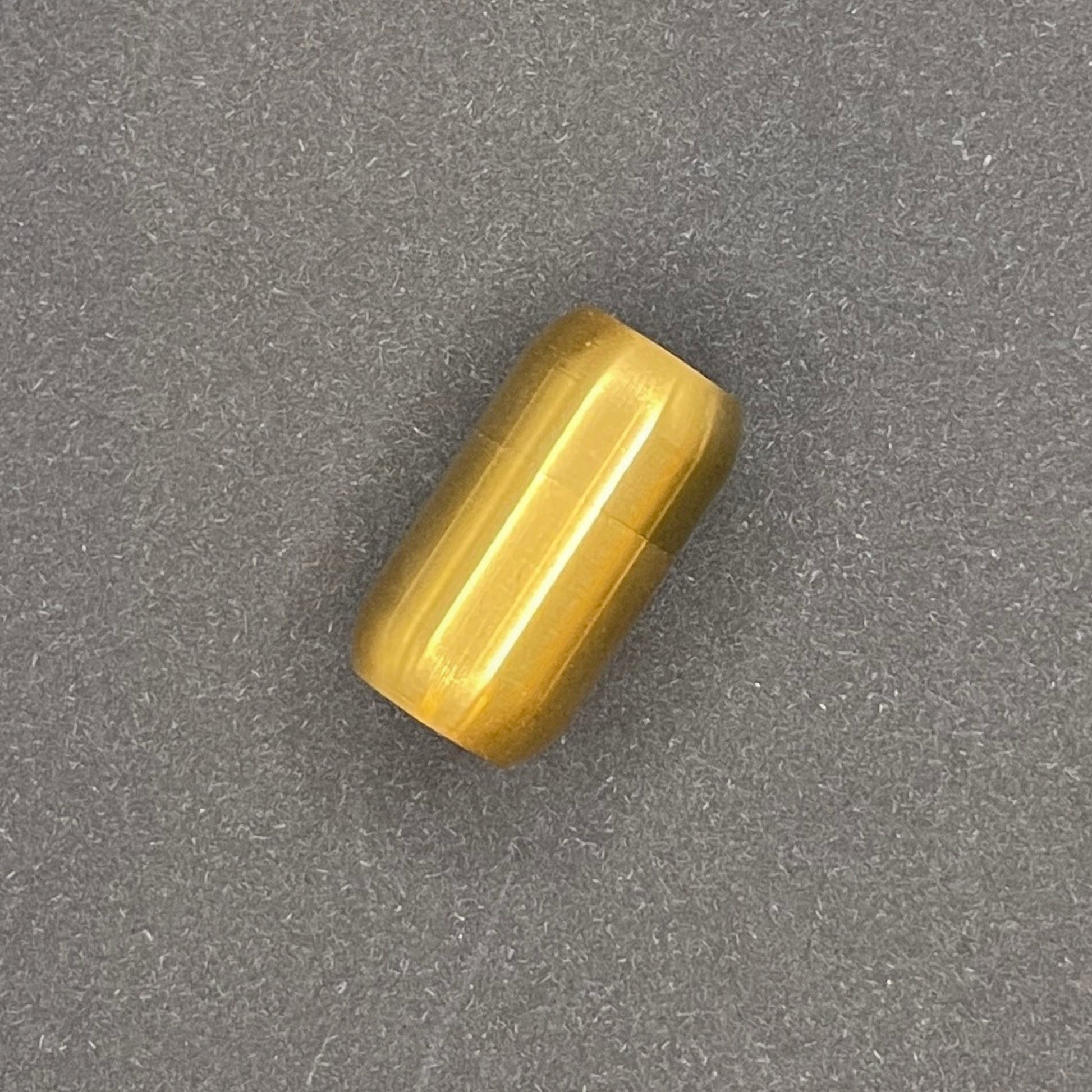 Gold cylindrical metal magnetic bracelet clasp, displayed on a dark textured background.