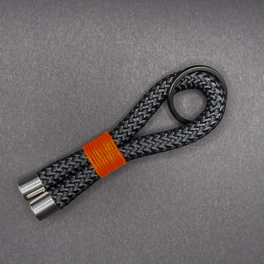 Flat lay of black braided rope keychain with silver end caps and orange whipping on a dark background.