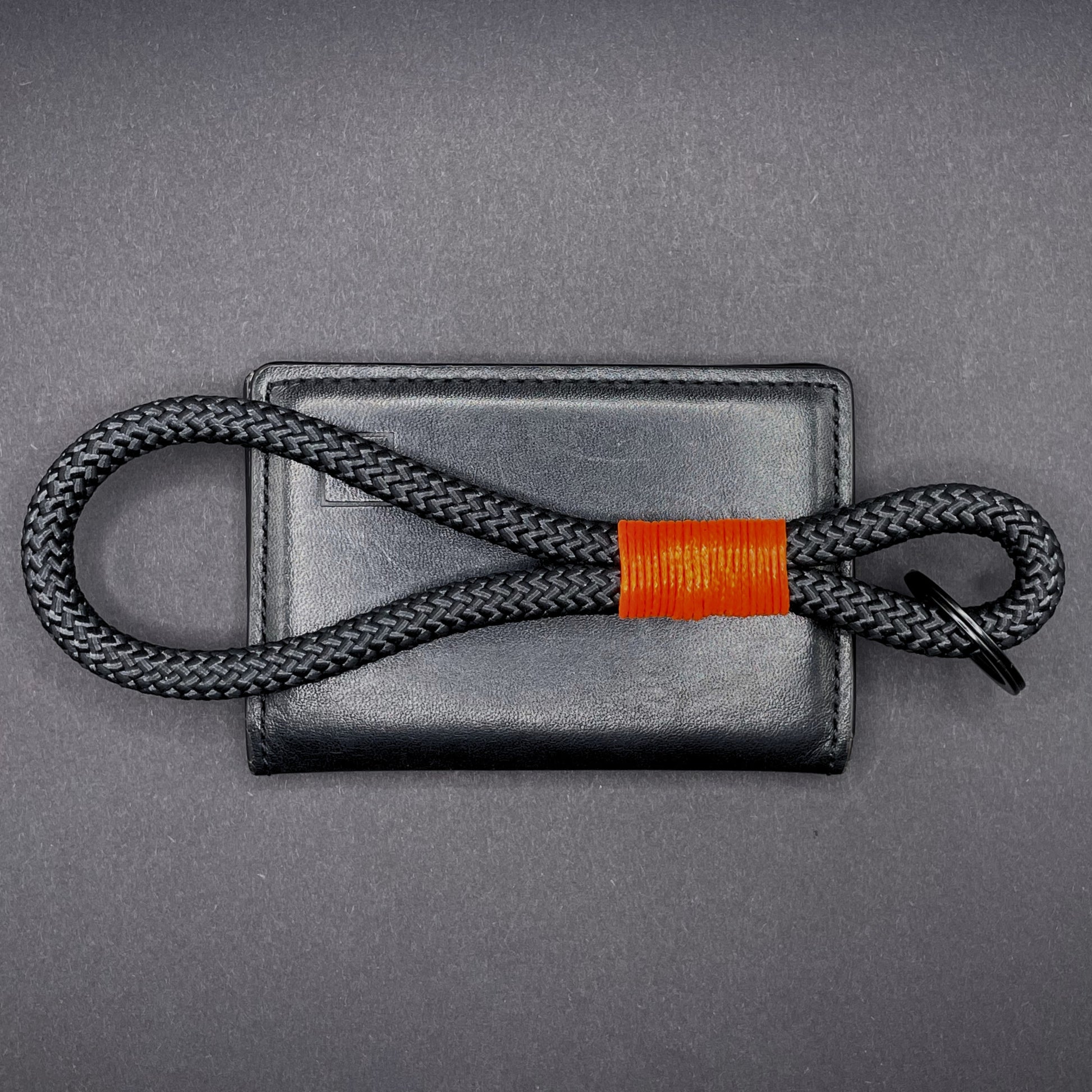 Black braided rope lanyard with a orange whipping detail, styled on a dark background.