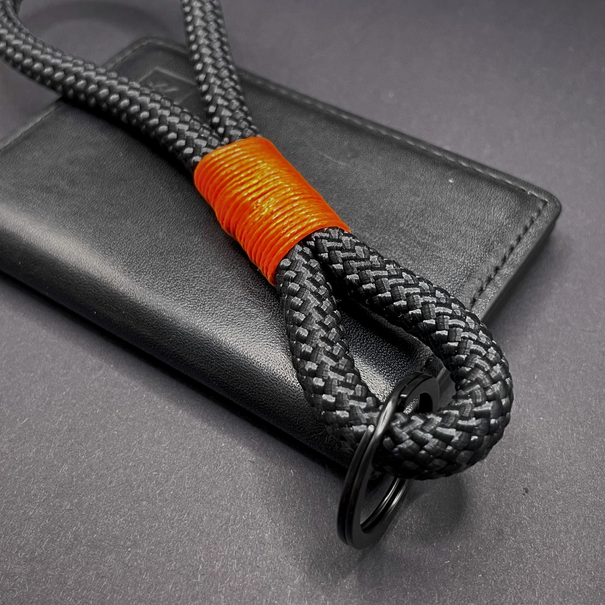Black braided rope lanyard with a orange whipping detail, styled on a dark background.