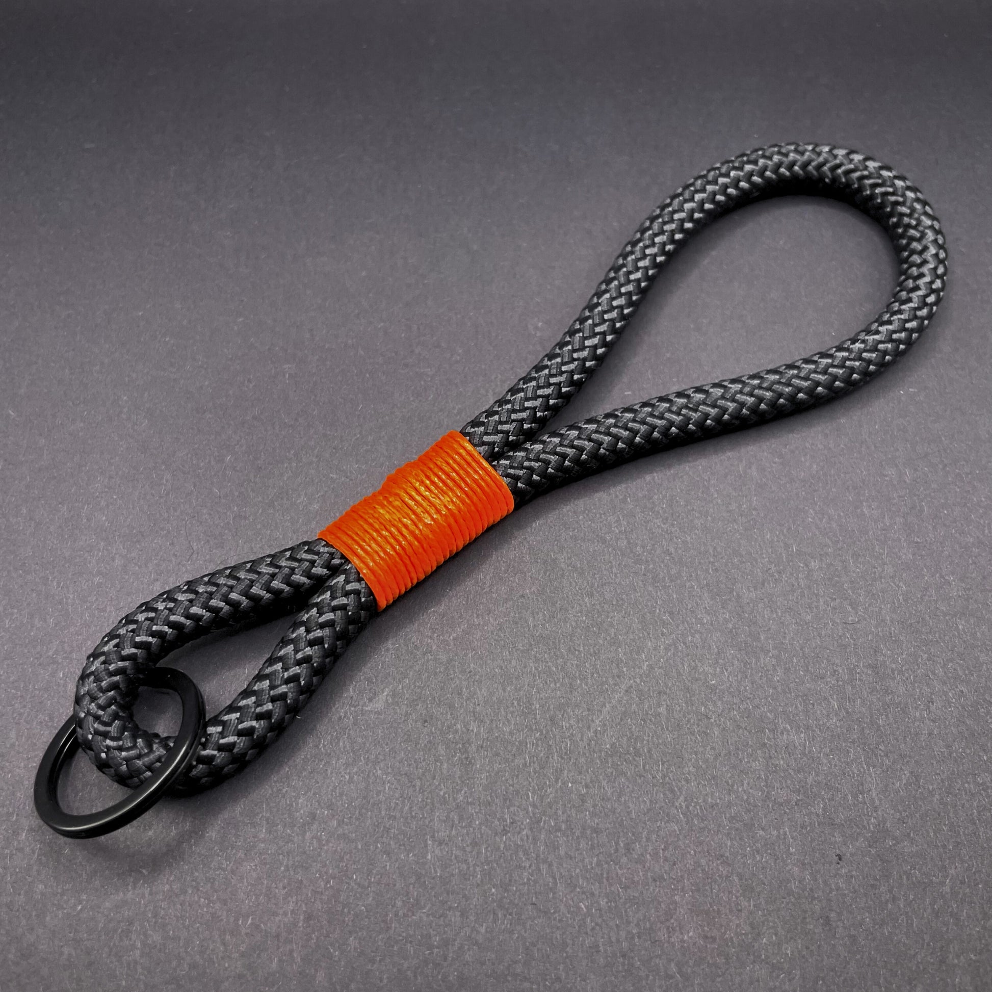 Black braided rope lanyard with a orange whipping detail, styled on a dark background.