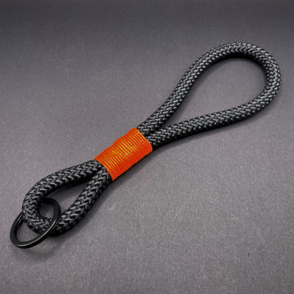 Black braided rope lanyard with a orange whipping detail, styled on a dark background.