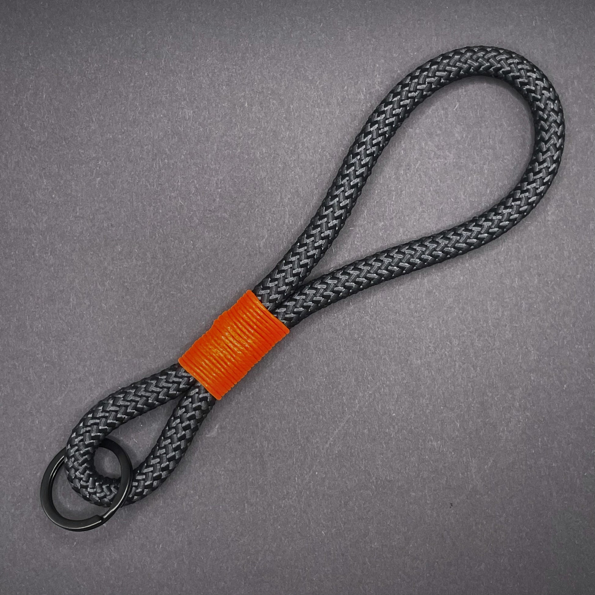 Black braided rope lanyard with a orange whipping detail, styled on a dark background.