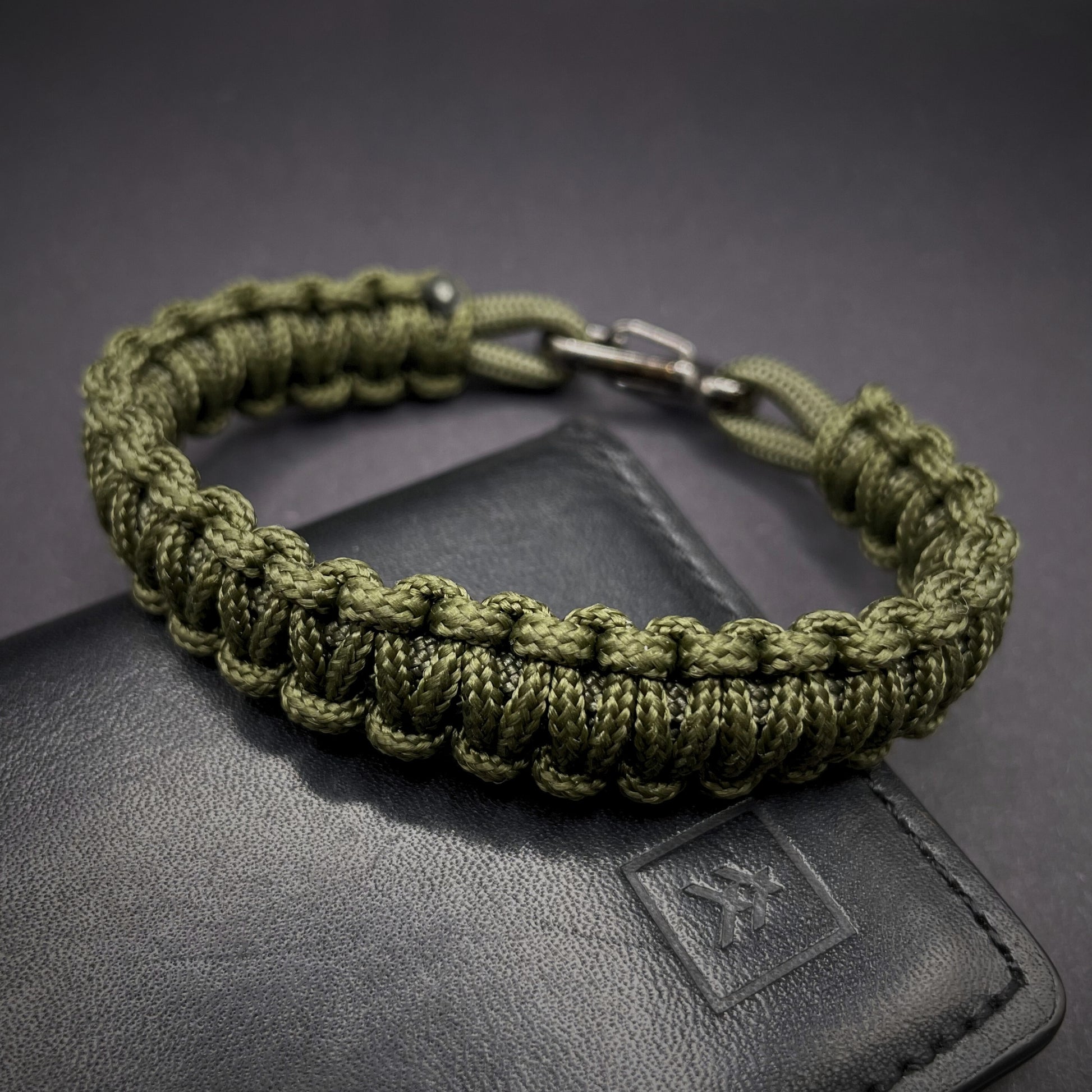 Flat lay of Army Green cobra knot paracord bracelet on a dark grey surface