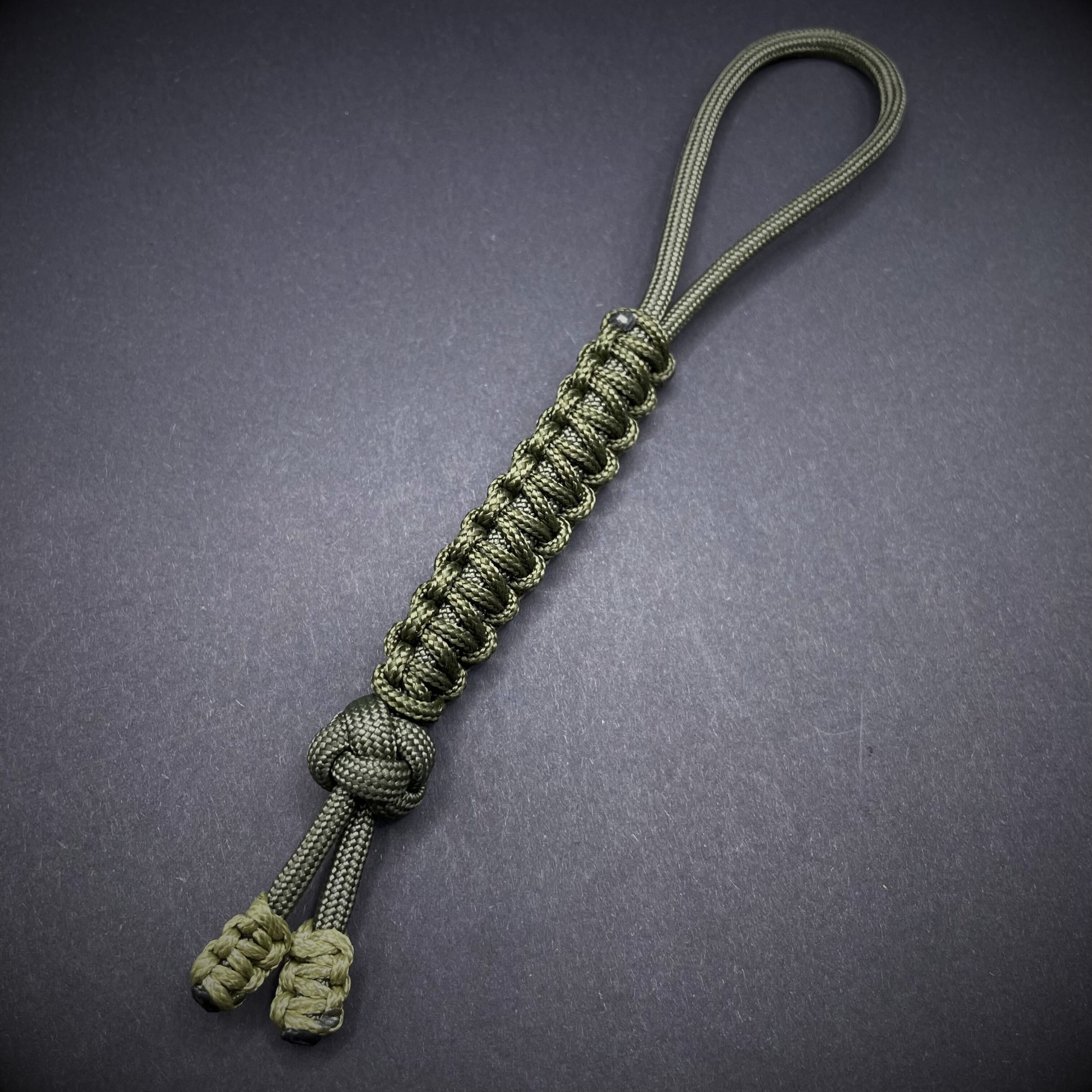 Flat lay of a army green 550 Paracord knife lanyards on a dark grey background