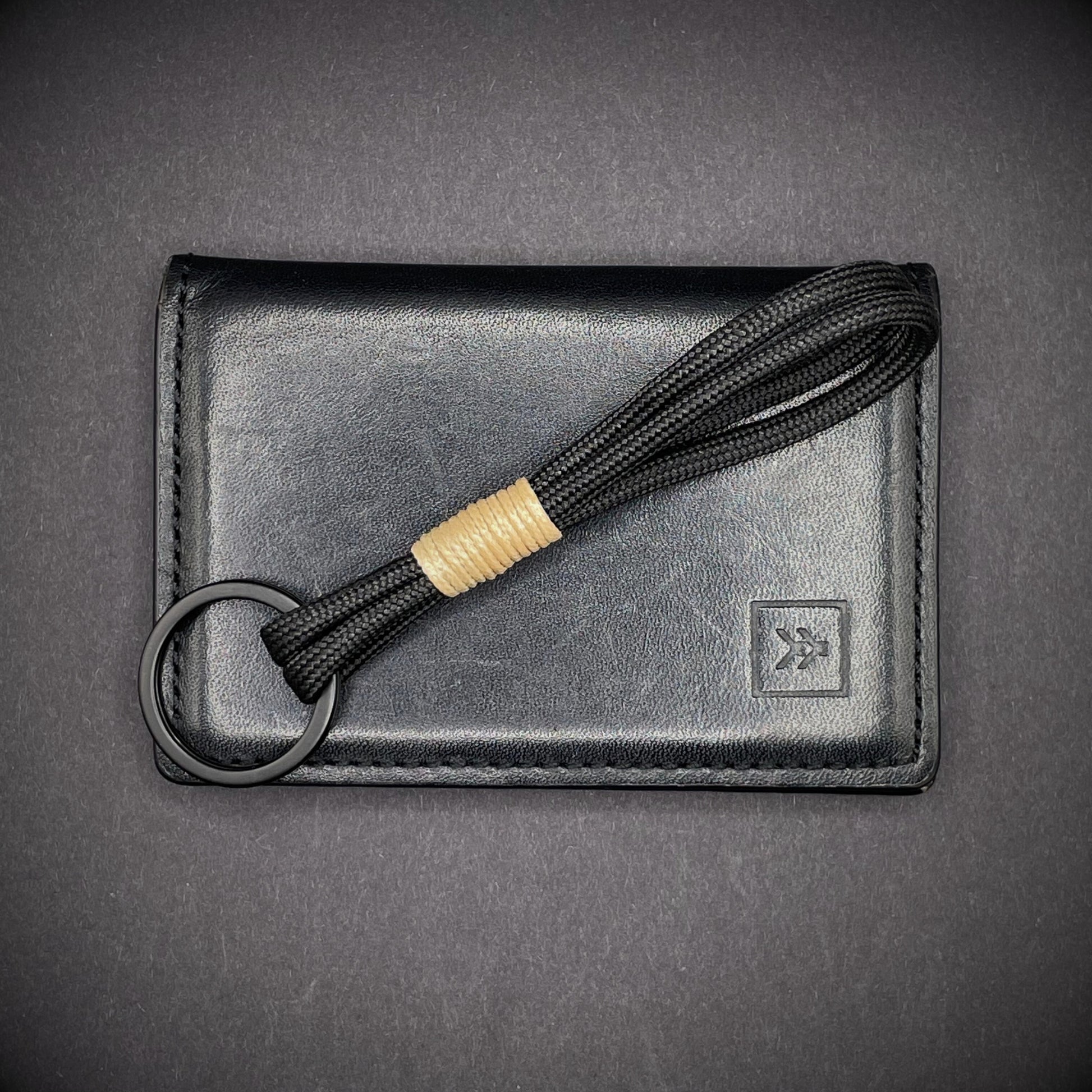 Flat lay of black 550 paracord keychain with tan cotton whipping on a dark background.