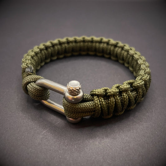 An army green paracord rope bracelet arranged on a dark grey surface.