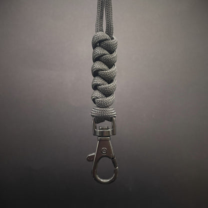 Black 550 Paracord snake knot lanyard with black lobster clasp, displayed on a dark textured background.