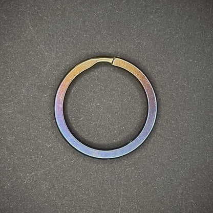 An Oil Slick Titanium Split Ring on a dark grey background
