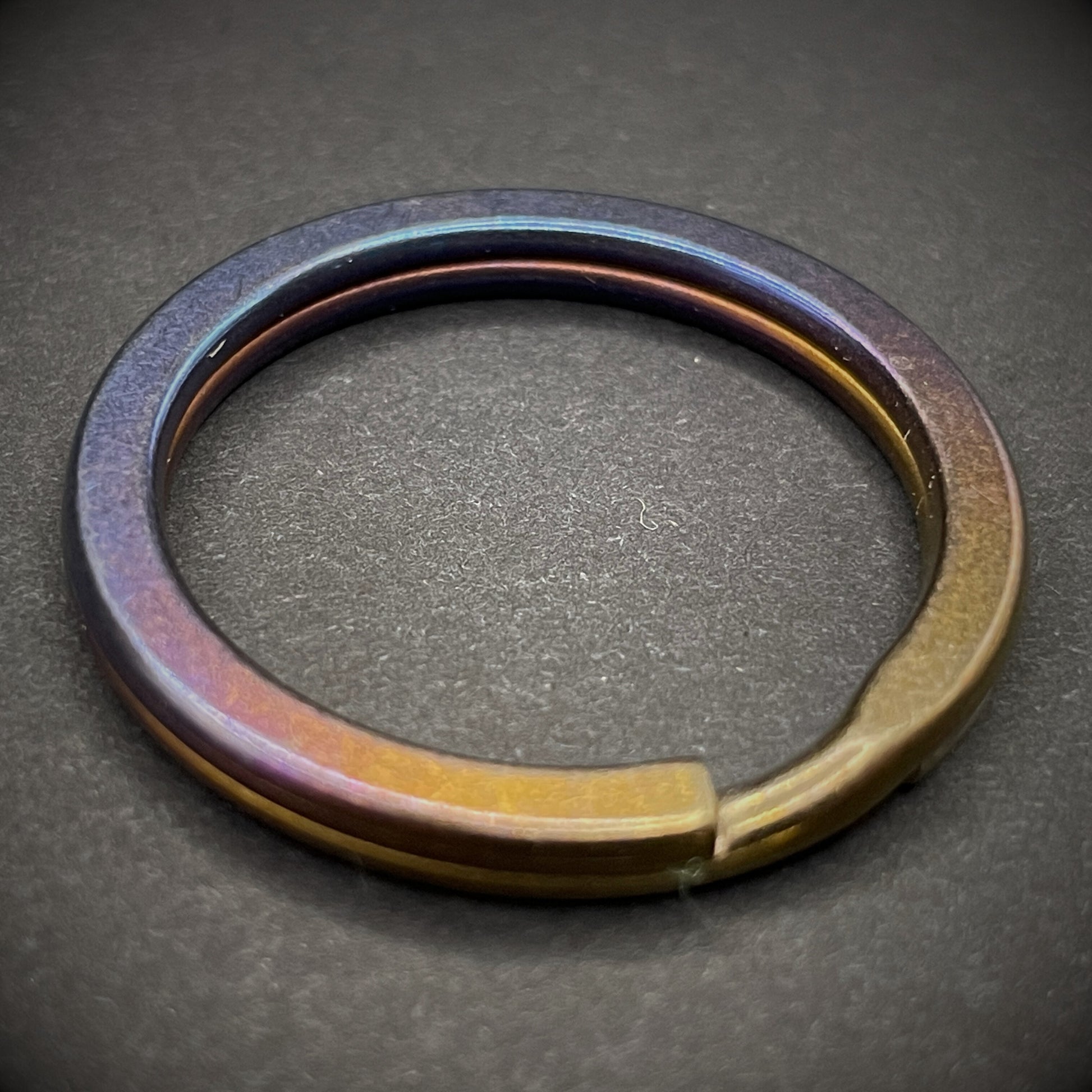 An Oil Slick Titanium Split Ring on a dark grey background