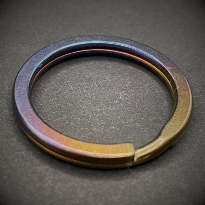 An Oil Slick Titanium Split Ring on a dark grey background