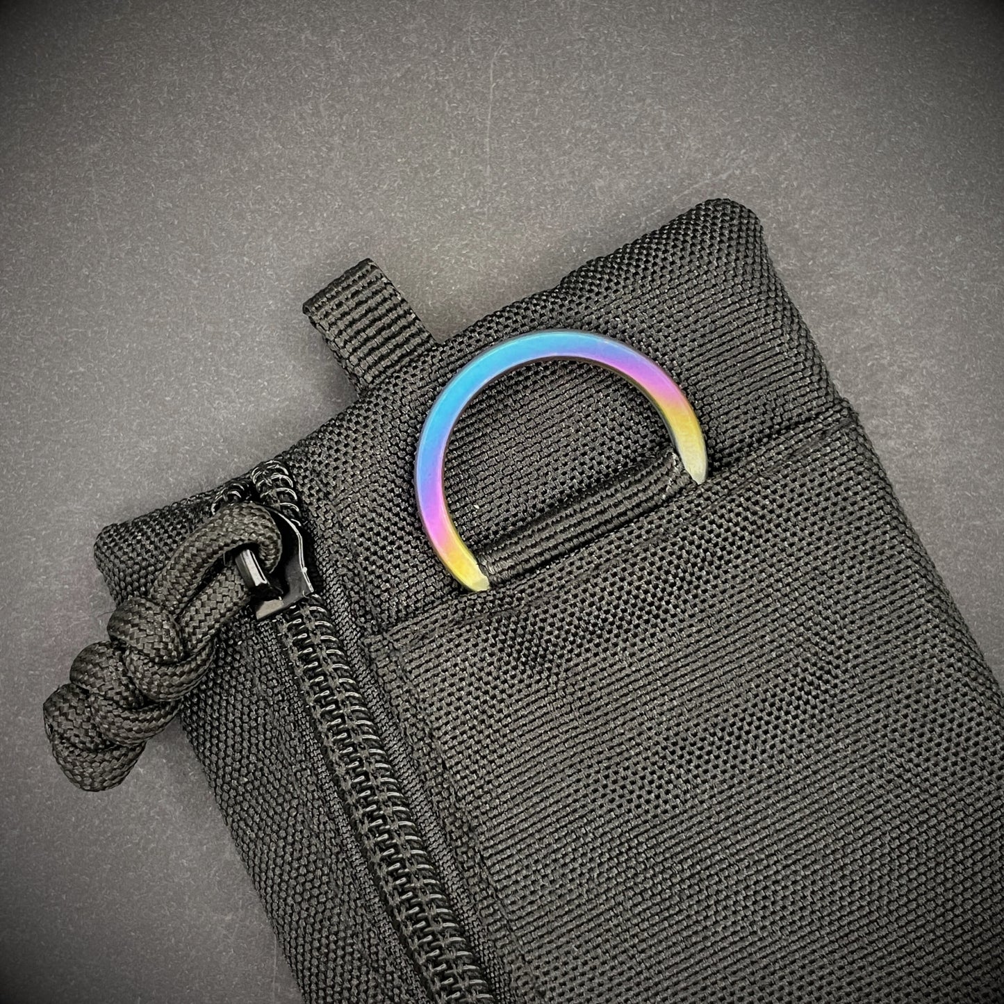 An Sunset Titanium Split Ring on a black pouch laid on a dark grey background