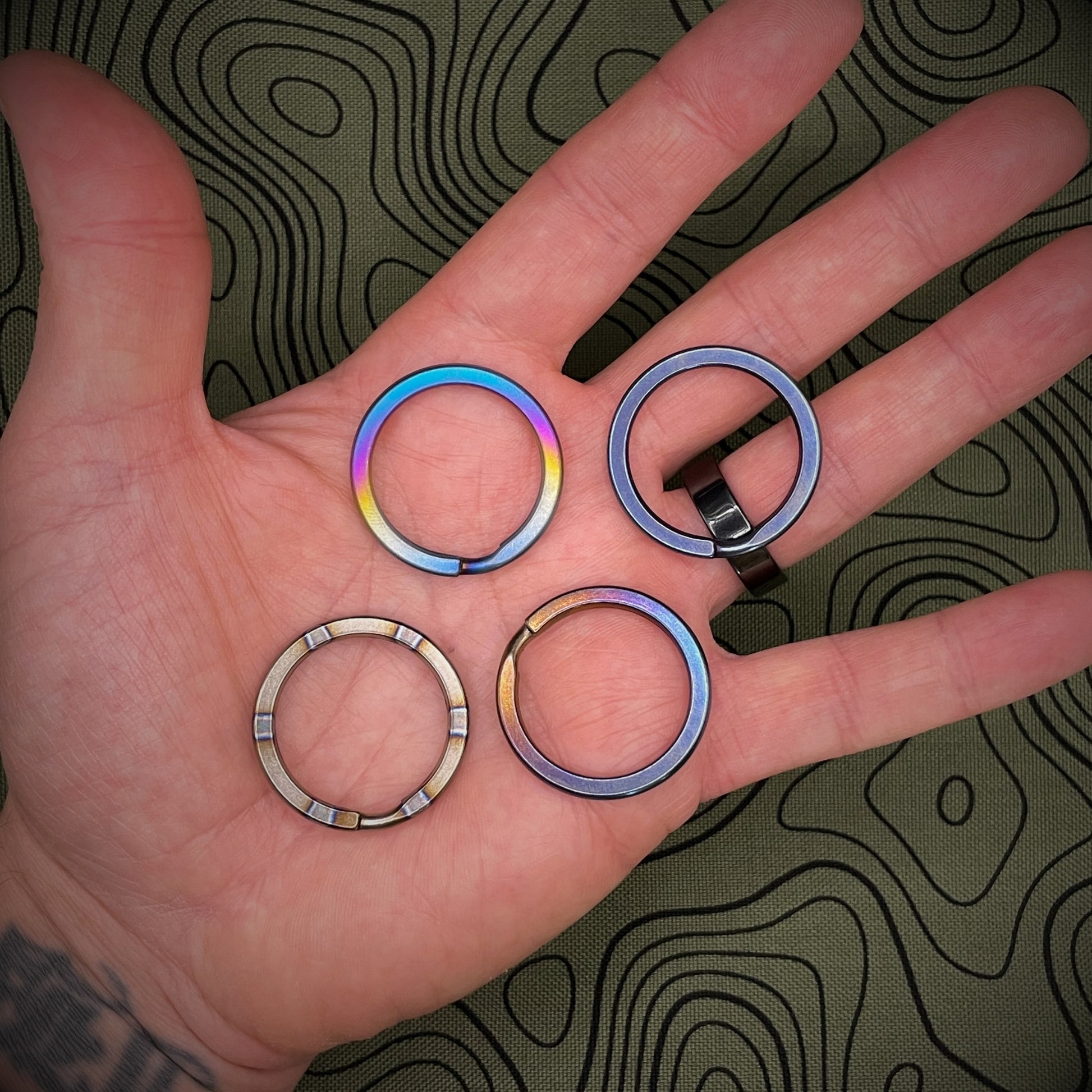 A group of Titanium Split Rings in the palm of an open hand above a topographical background