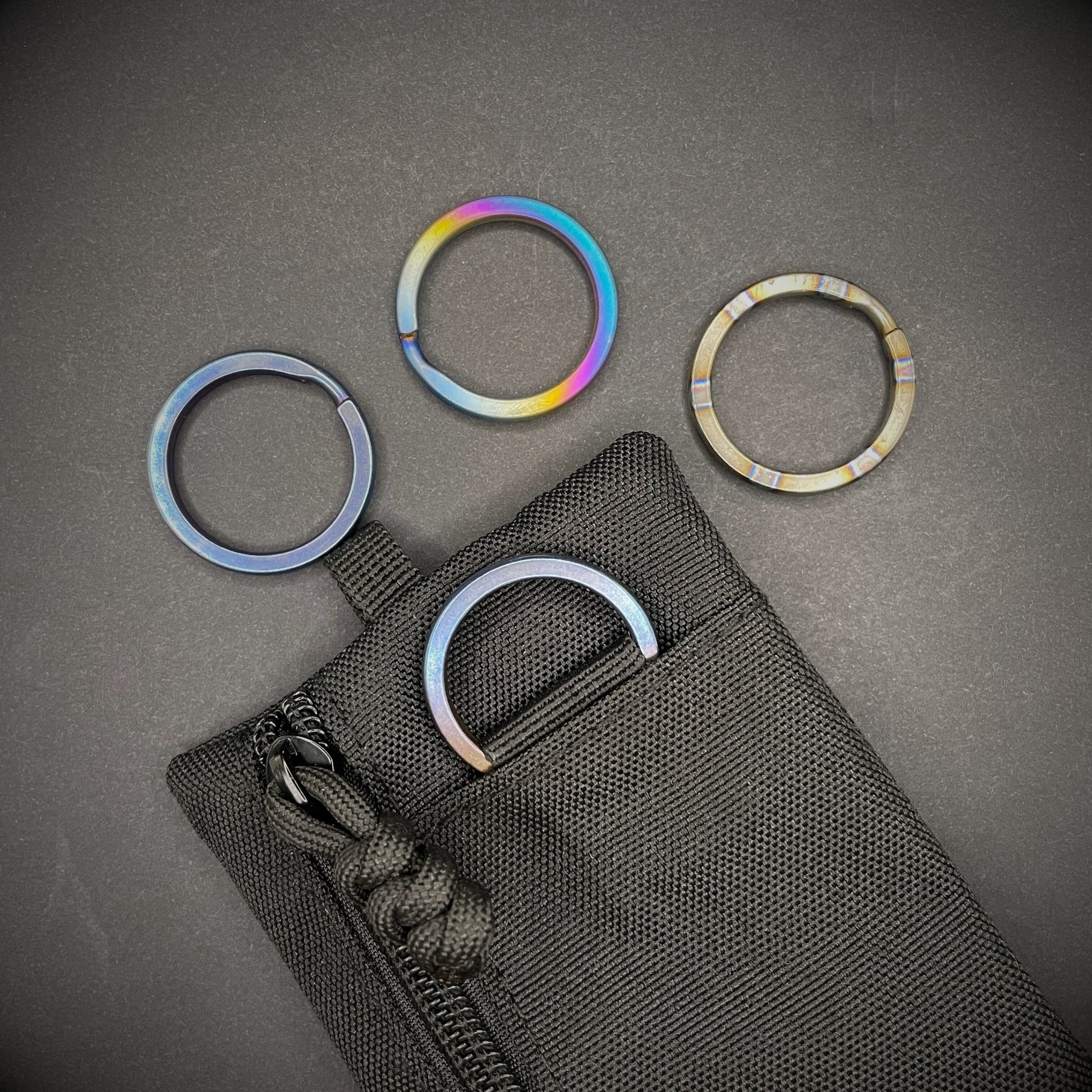 A group of Titanium Split Rings on a dark grey background, one is attached to a black pouch