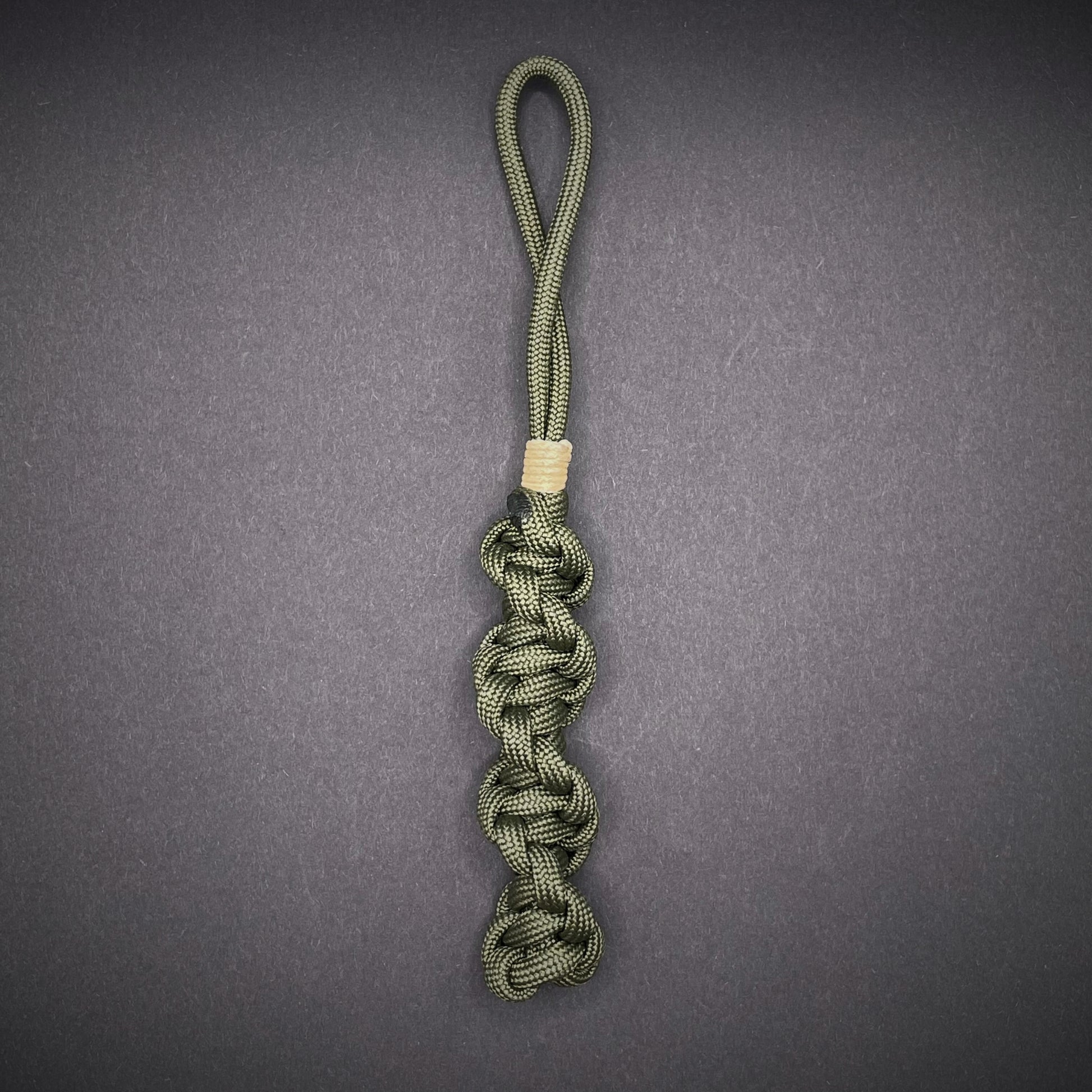 Flat lay of an Army Green 550 Paracord knife lanyards on a dark grey background