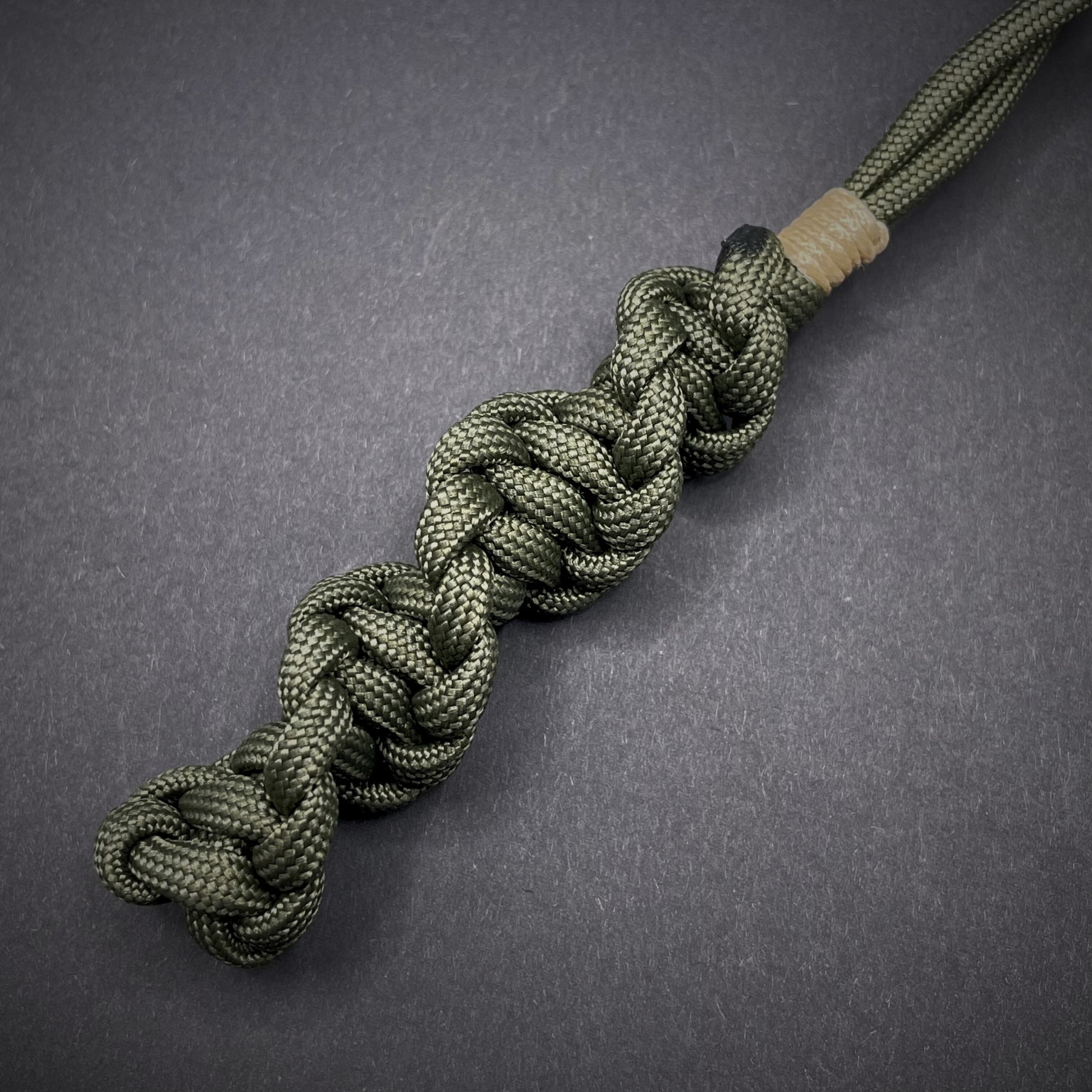 Flat lay of an Army Green 550 Paracord knife lanyards on a dark grey background