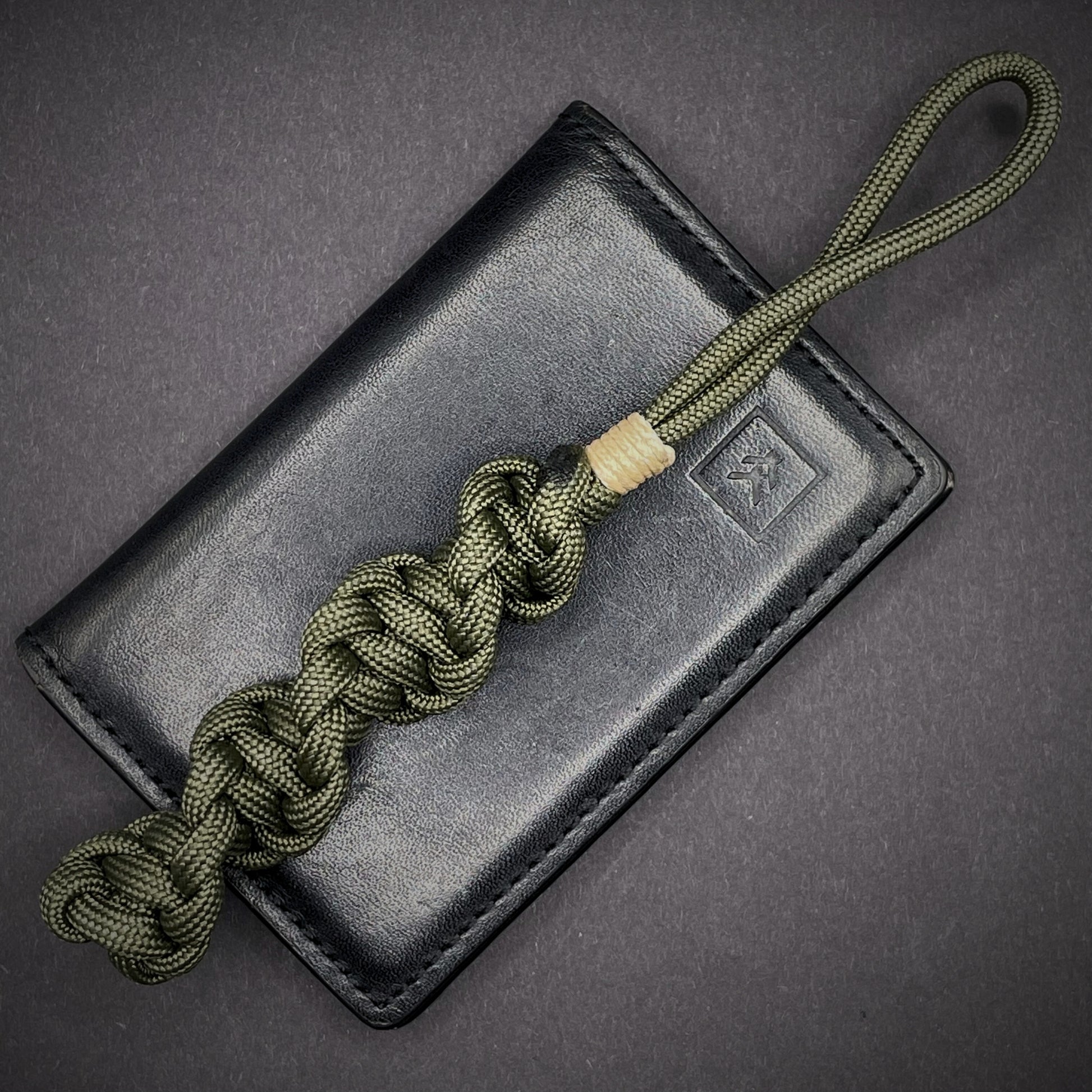 Flat lay of an Army Green 550 Paracord knife lanyards on a dark grey background