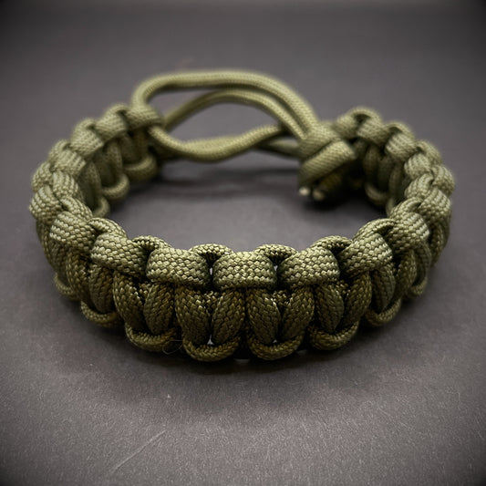 An Army green 550 paracord cobra knot bracelet displayed on a dark grey surface.